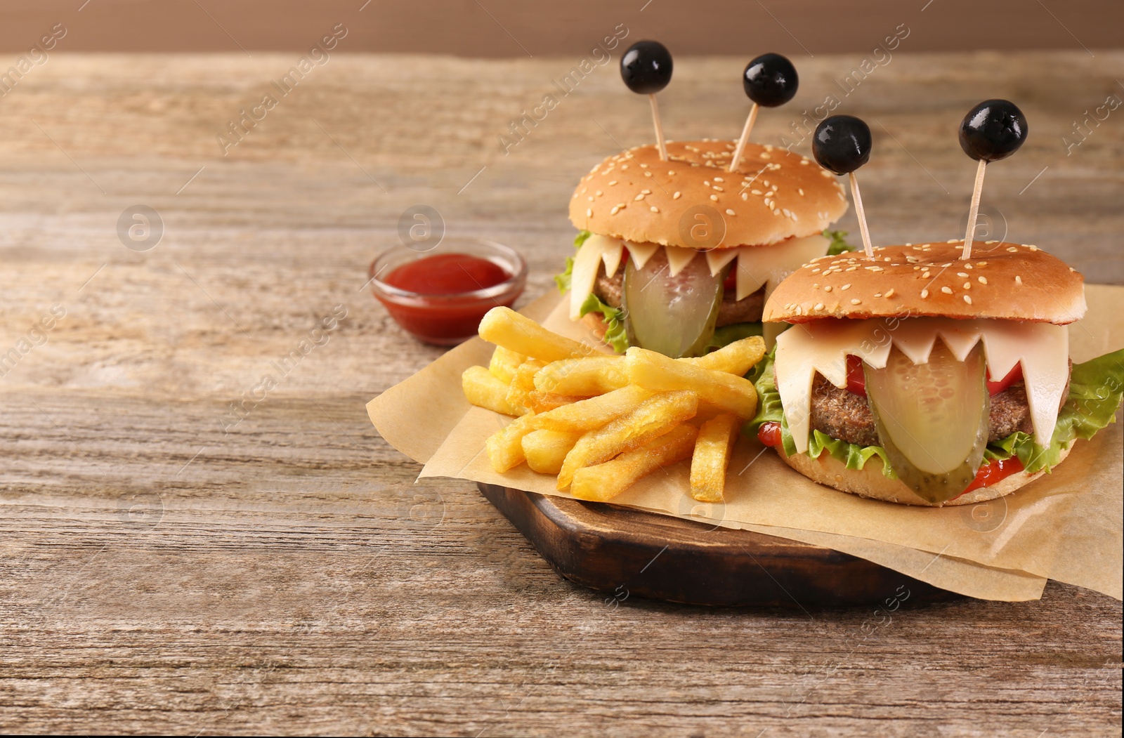 Photo of Cute monster burgers served with french fries and ketchup on wooden table, space for text. Halloween party food