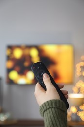 Photo of Woman with remote control in room decorated for Christmas, closeup