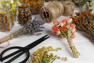 Different medicinal herbs, scissors and spools on white wooden table
