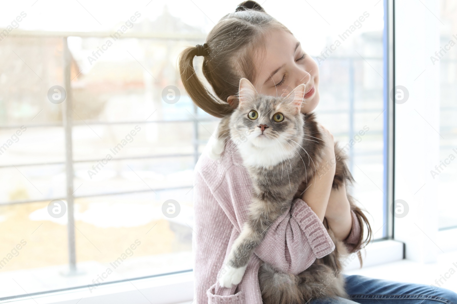 Photo of Cute little girl with cat near window at home