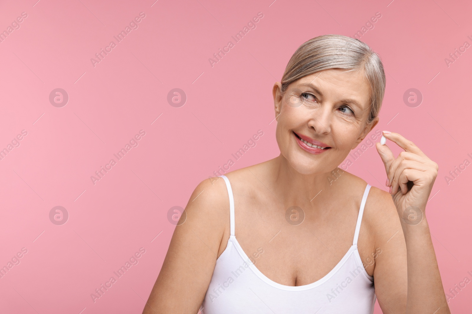 Photo of Beautiful woman with vitamin pill on pink background, space for text