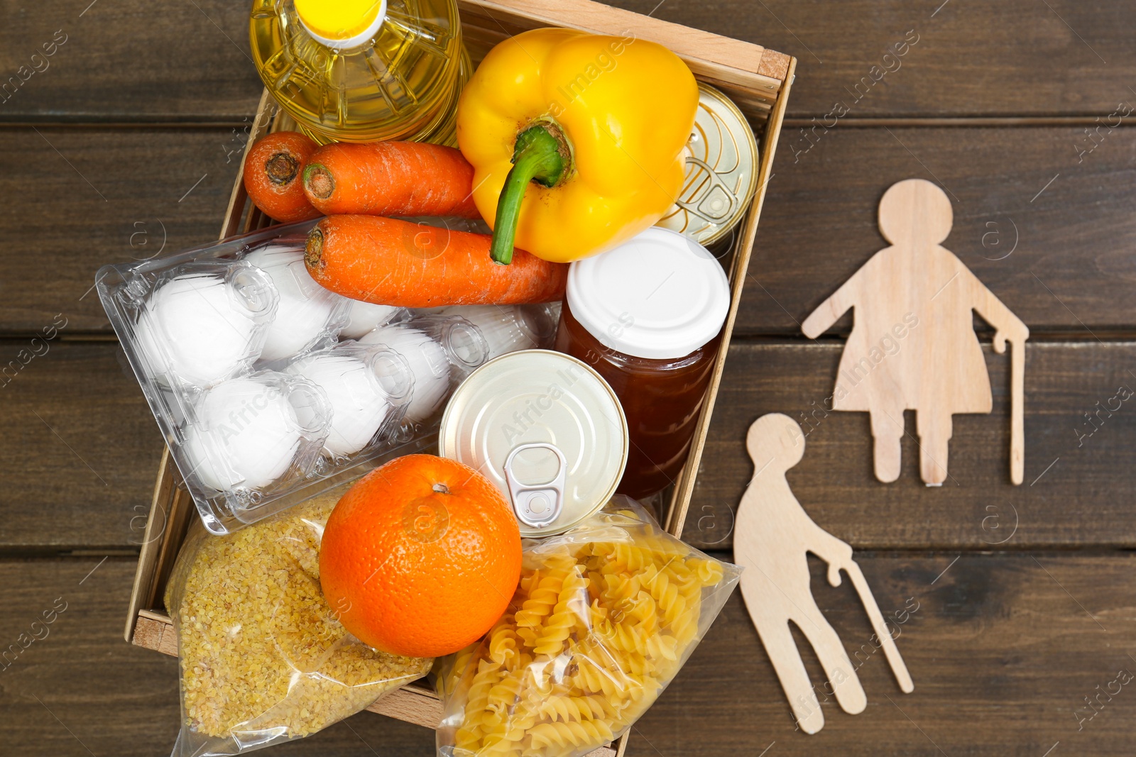 Photo of Humanitarian aid for elderly people. Crate with donation food and figures of couple on wooden table, top view