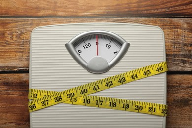 Photo of Weigh scales tied with measuring tape on wooden table, top view. Overweight concept