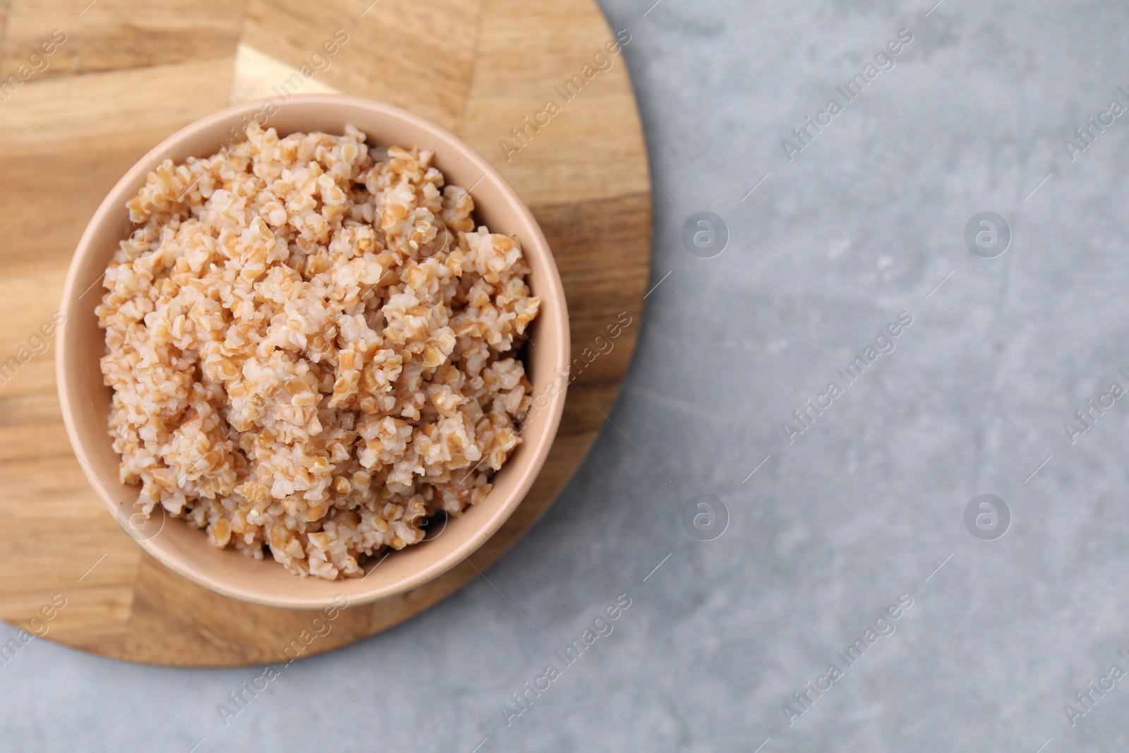 Photo of Tasty wheat porridge in bowl on grey table, top view. Space for text