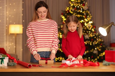 Christmas presents wrapping. Mother and her little daughter decorating gift boxes at home