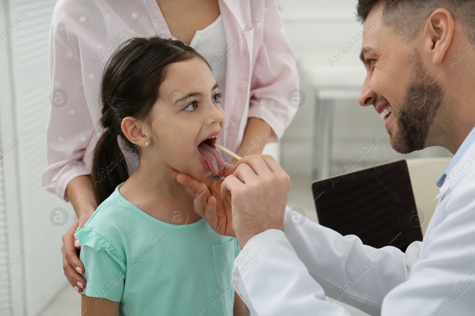 Photo of Mother with daughter visiting pediatrician in hospital. Doctor examining little girl