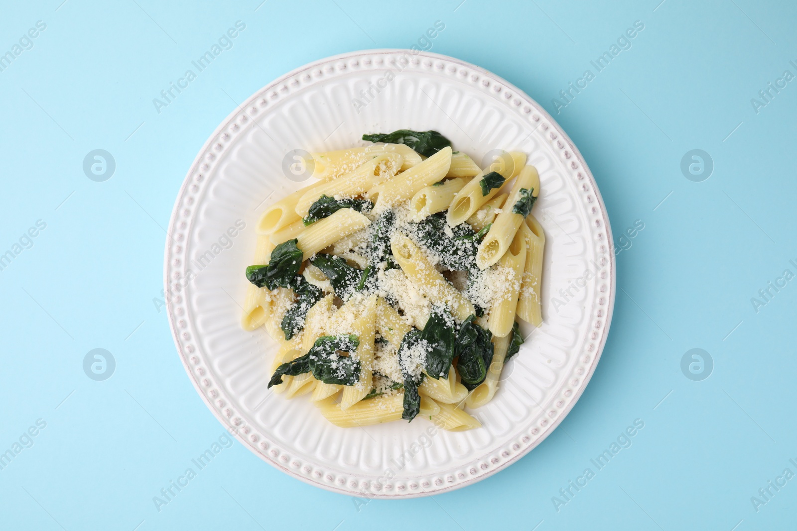 Photo of Tasty pasta with spinach and cheese on light blue table, top view