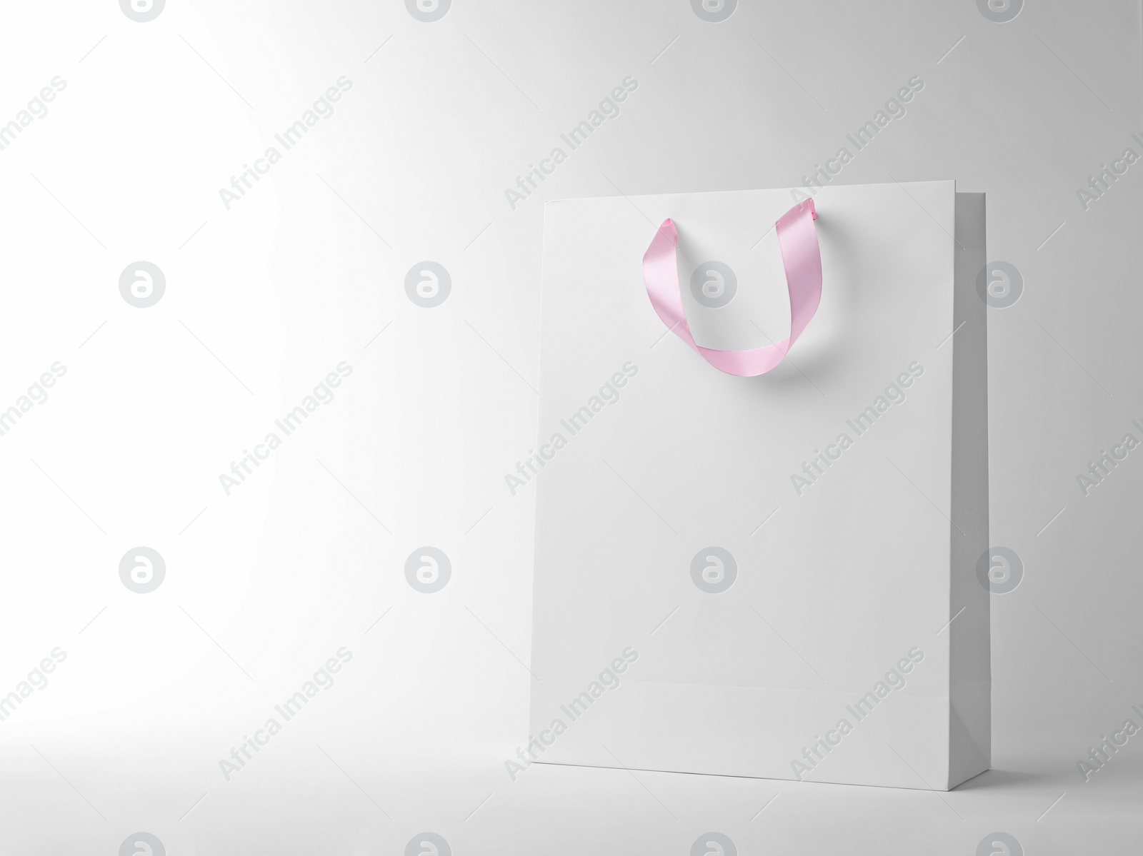 Photo of Paper shopping bag with ribbon handles on white background. Mockup for design