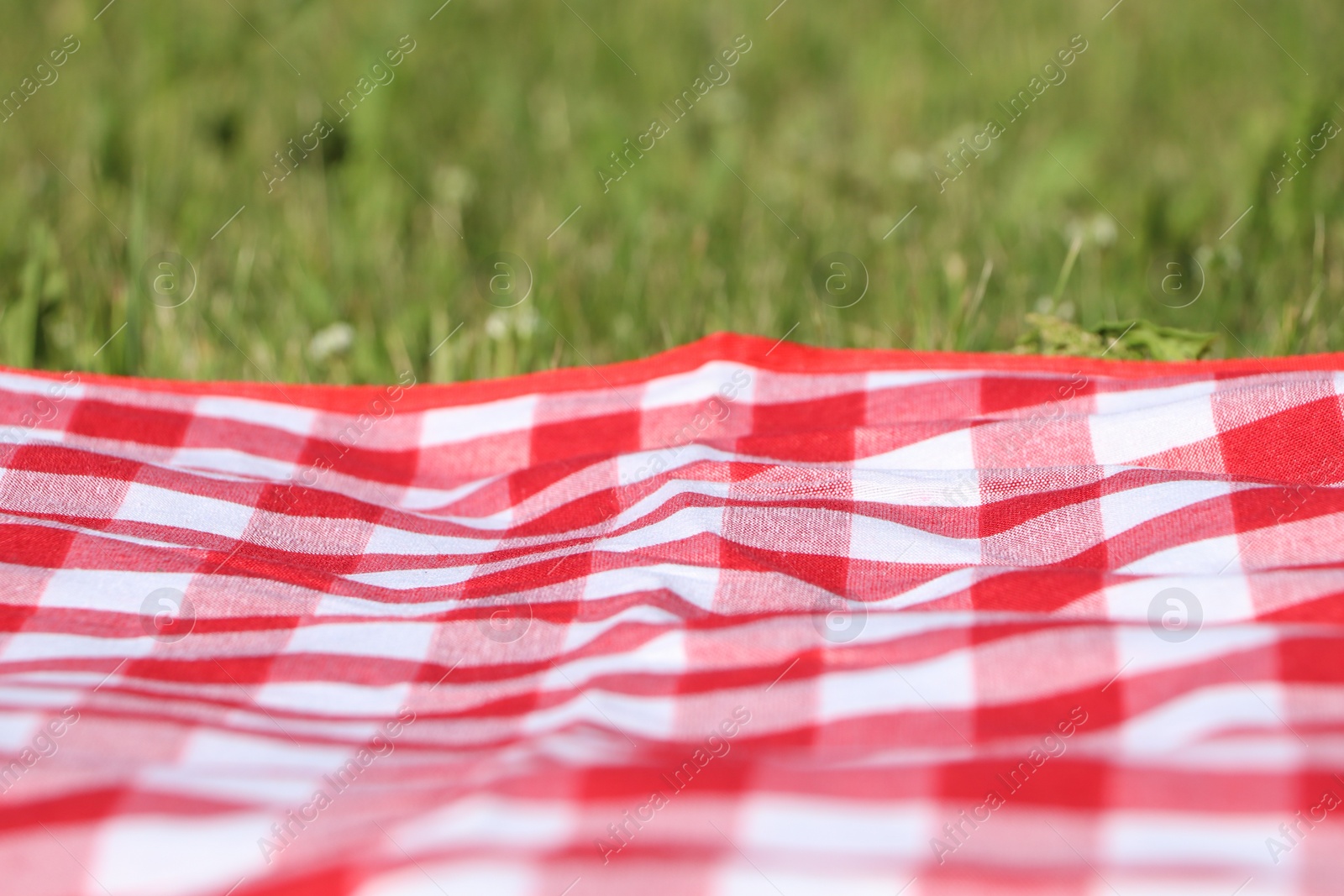 Photo of Checkered picnic tablecloth on fresh green grass, closeup