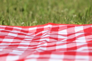 Checkered picnic tablecloth on fresh green grass, closeup