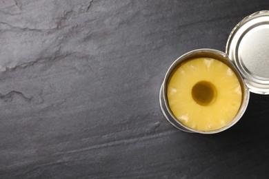 Tin with canned pineapple on black slate table, top view. Space for text