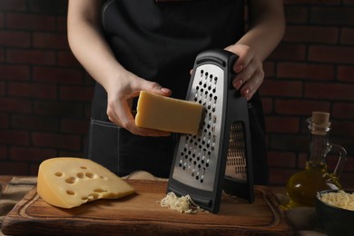 Woman grating cheese at wooden table, closeup