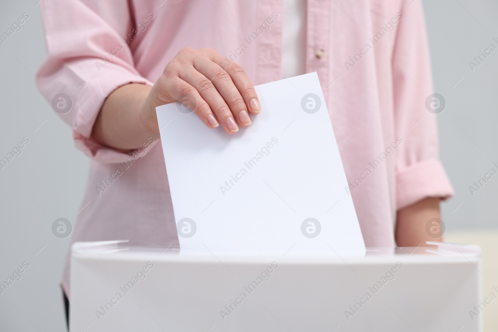 Photo of Woman putting her vote into ballot box on blurred background, closeup