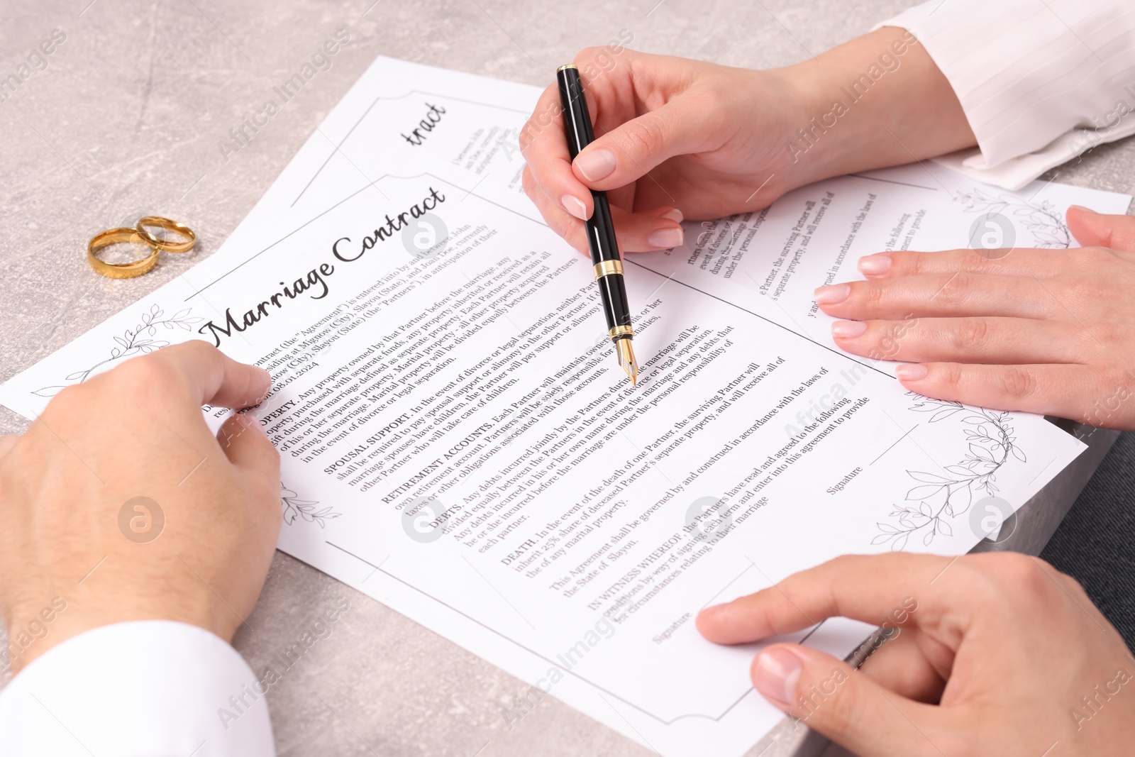 Photo of Man and woman signing marriage contract at light grey table, closeup