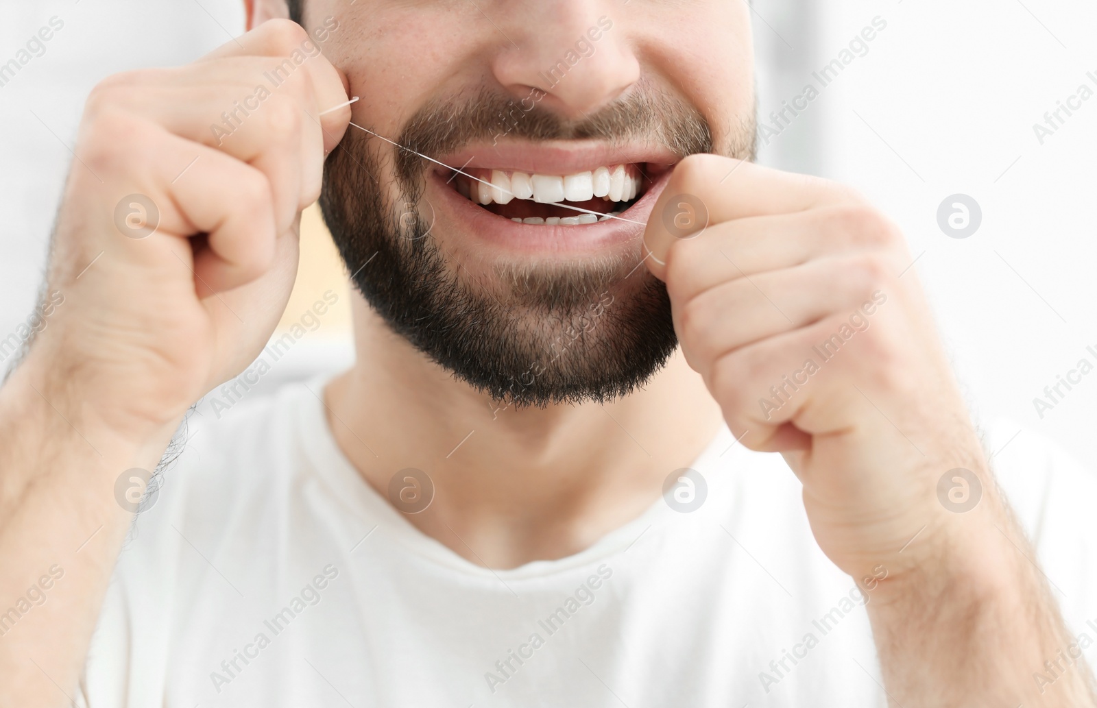 Photo of Young man flossing his teeth indoors