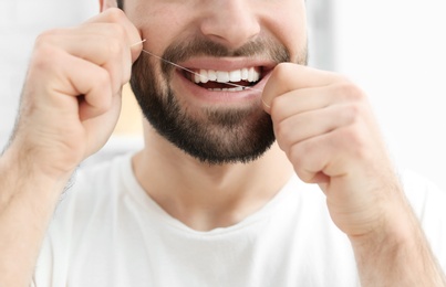 Photo of Young man flossing his teeth indoors