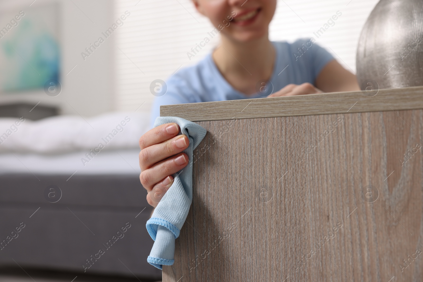 Photo of Woman with microfiber cloth cleaning wooden chest of drawers in room, closeup