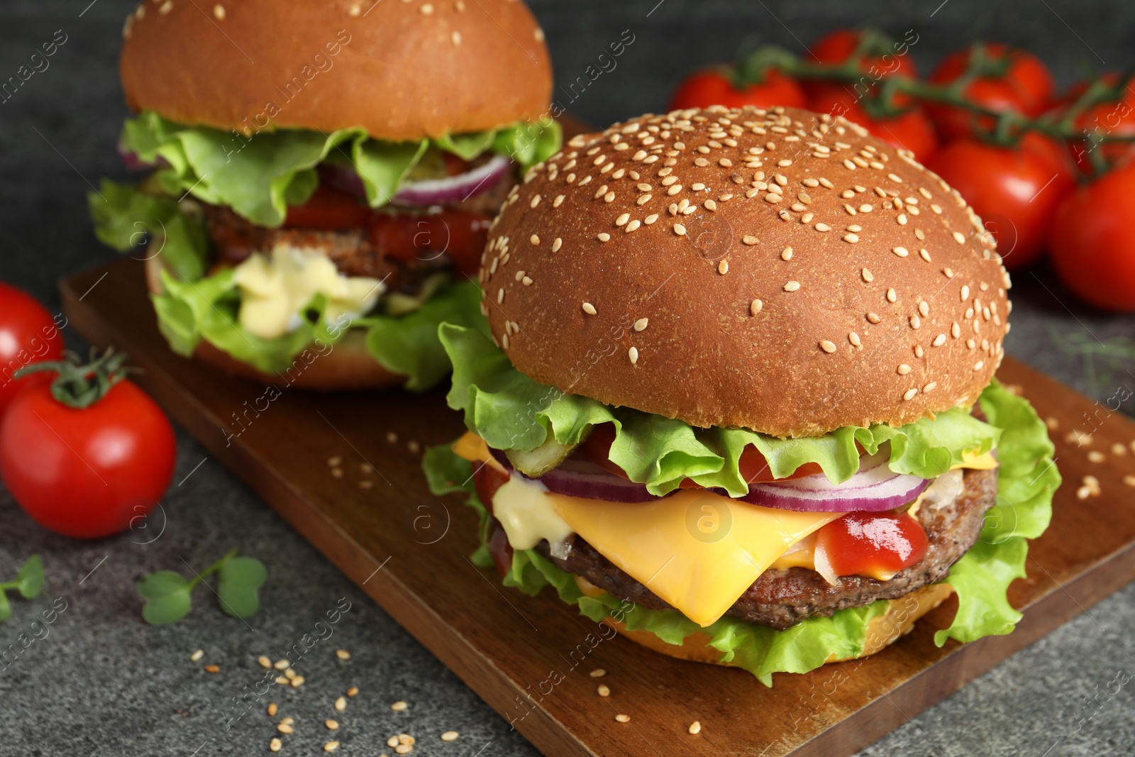 Photo of Delicious burgers with beef patty and tomatoes on grey table, closeup