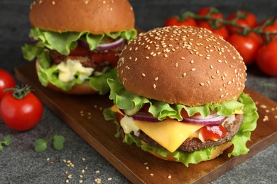 Photo of Delicious burgers with beef patty and tomatoes on grey table, closeup