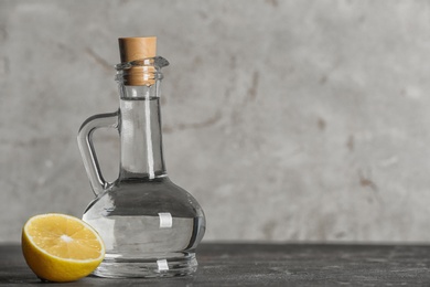 Photo of Glass jug with vinegar and lemon on table. Space for text