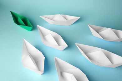 Photo of Group of paper boats following green one on light blue background. Leadership concept