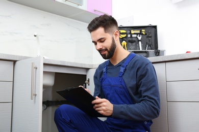 Male plumber with clipboard near kitchen sink. Repair service