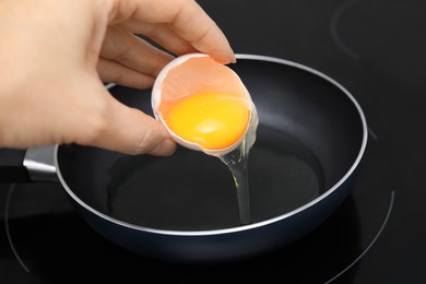 Photo of Woman adding raw egg into frying pan, closeup