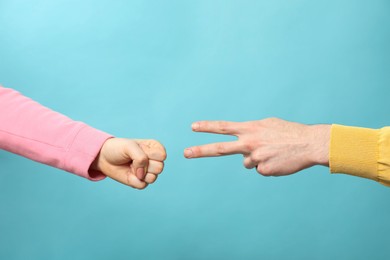 People playing rock, paper and scissors on light blue background, closeup