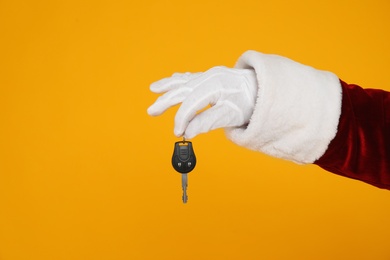 Photo of Santa Claus holding car key on yellow background, closeup of hand