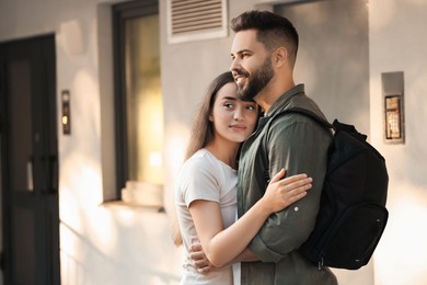 Photo of Long-distance relationship. Man with backpack hugging with his girlfriend near house entrance outdoors