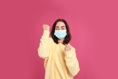 Photo of Emotional woman with protective mask on pink background. Strong immunity concept