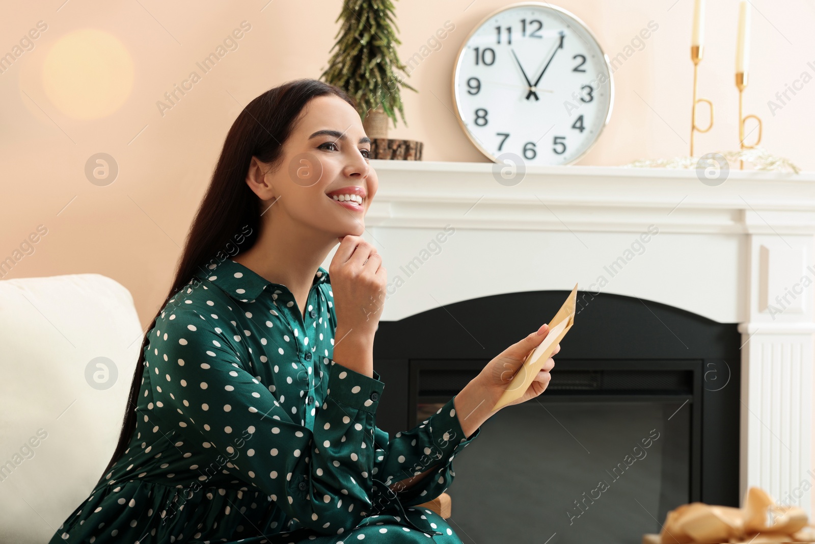 Photo of Happy woman holding Christmas greeting card in living room