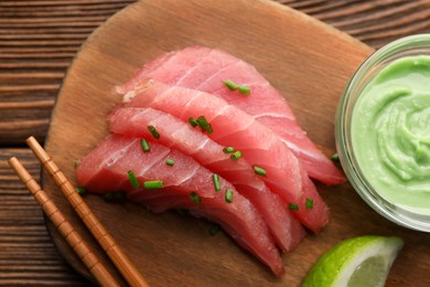 Photo of Tasty sashimi (pieces of fresh raw tuna) served with wasabi sauce and lime wedge on wooden board, top view
