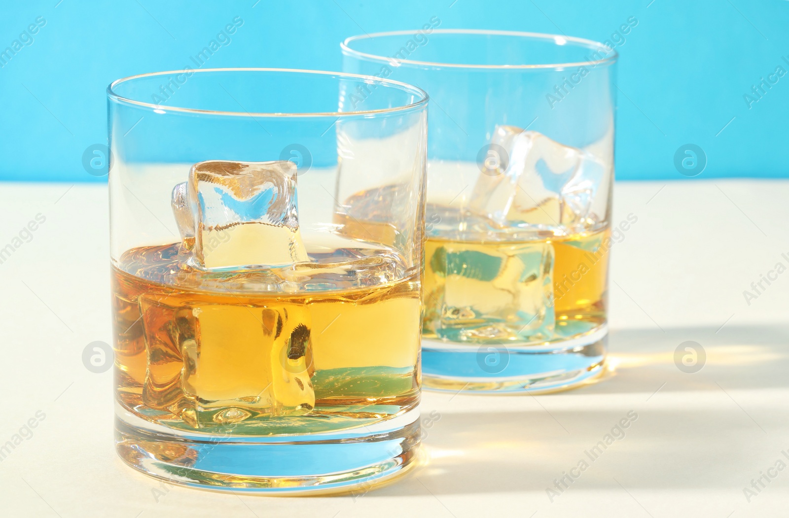 Photo of Whiskey with ice cubes in glasses on white table, closeup