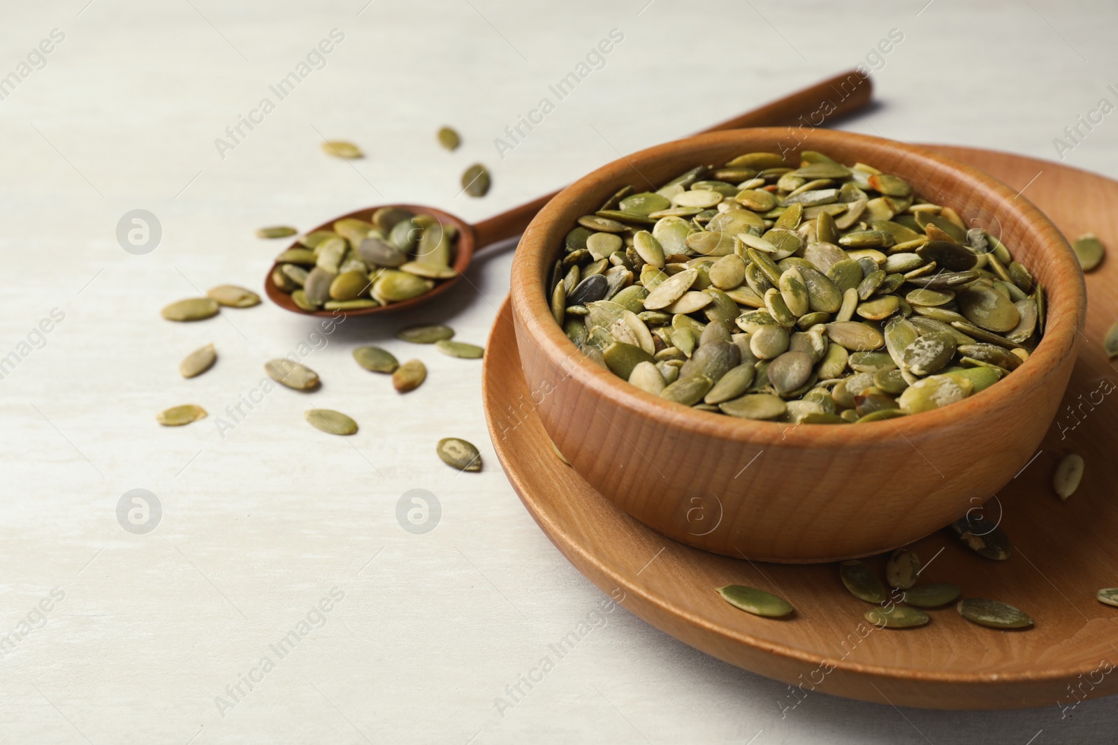 Photo of Shelled raw pumpkin seeds in dish on light background