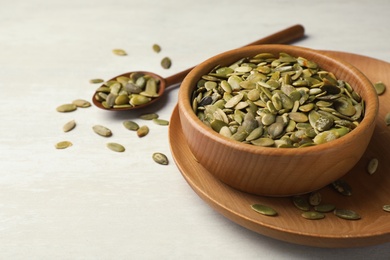 Photo of Shelled raw pumpkin seeds in dish on light background