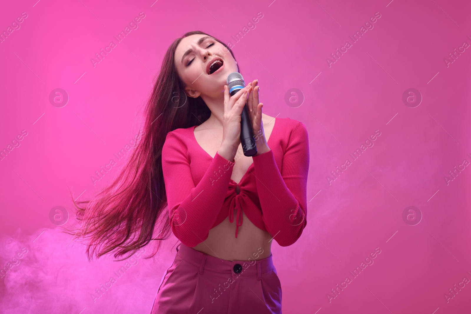 Photo of Emotional woman with microphone singing on pink background