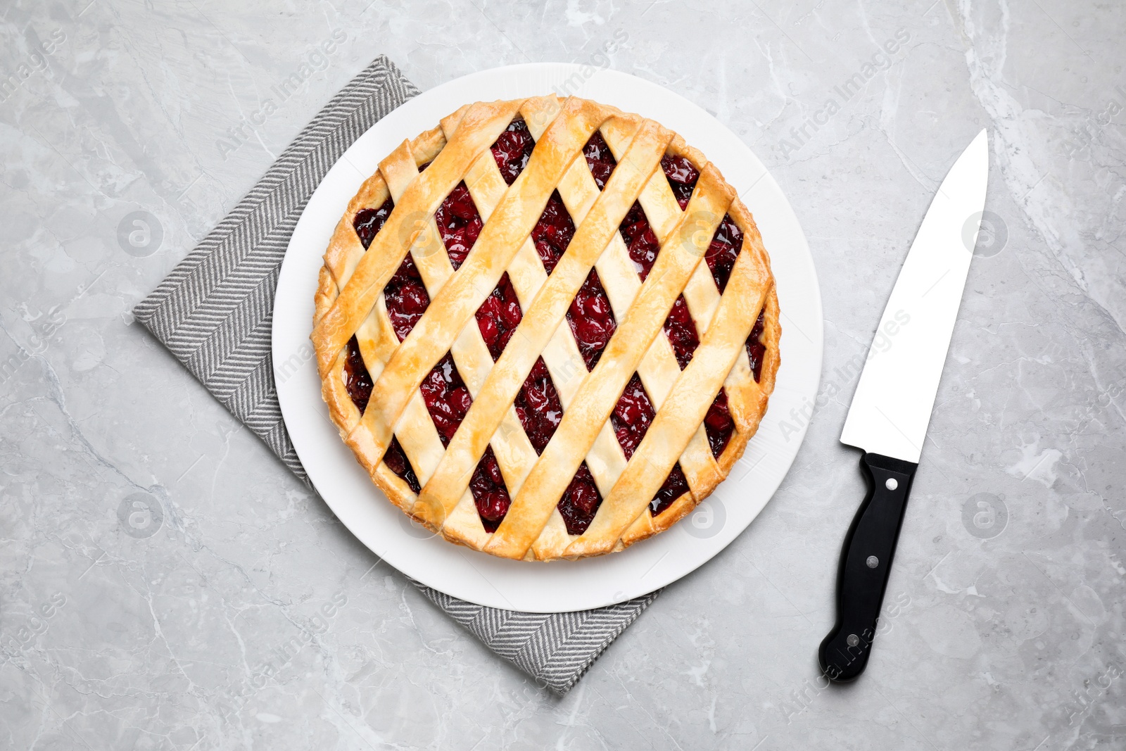 Photo of Delicious fresh cherry pie and knife on light grey table, flat lay