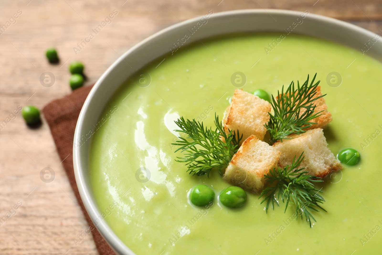 Photo of Fresh vegetable detox soup made of green peas with croutons in dish on table, closeup