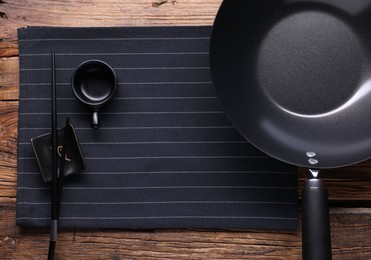 Empty iron wok, sauce bowl and chopsticks on wooden table, flat lay