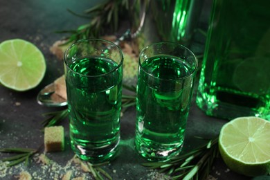 Photo of Absinthe in shot glasses, lime, rosemary and sugar on gray table, closeup. Alcoholic drink