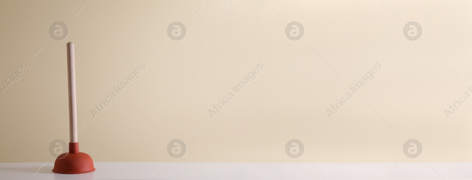 Photo of Plunger on white table against beige background. Space for text