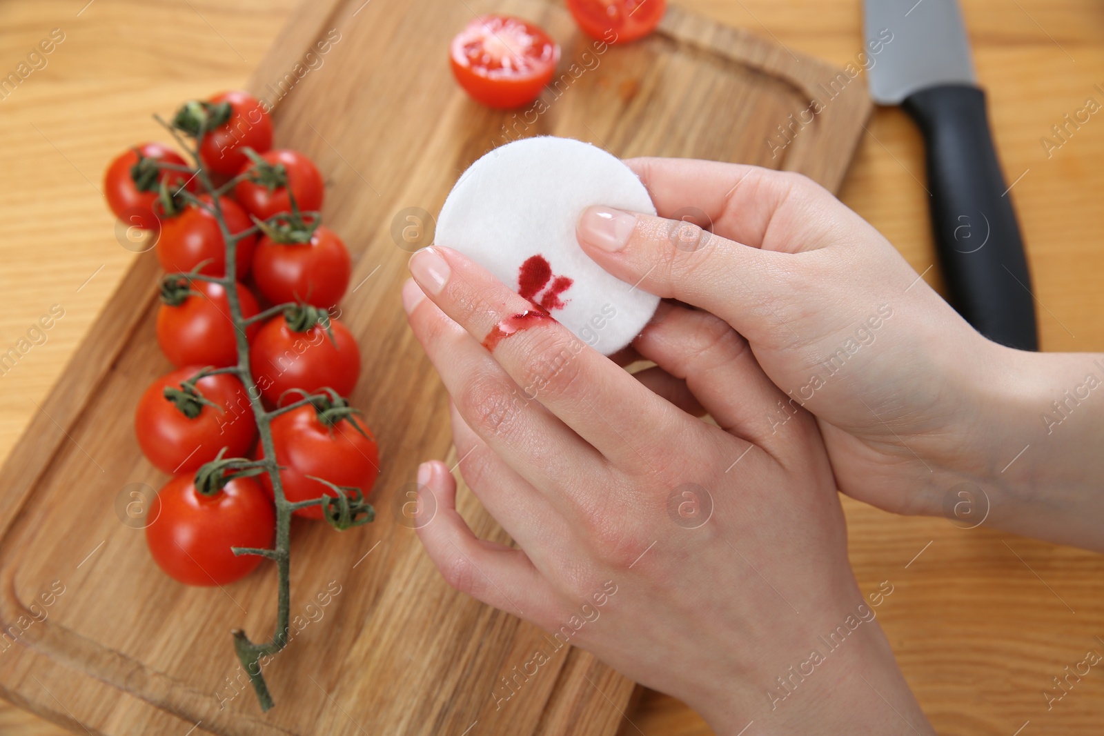 Photo of Woman cut finger while cooking at wooden table, closeup