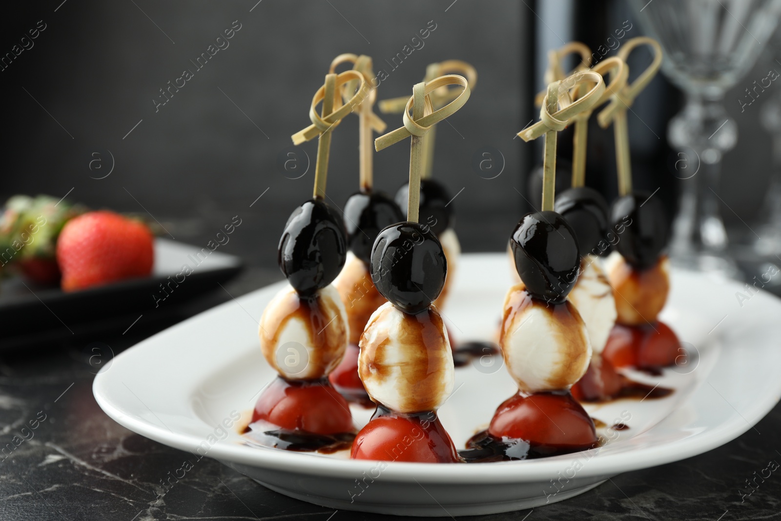 Photo of Tasty canapes with black olives, mozzarella and cherry tomatoes on dark textured table, closeup