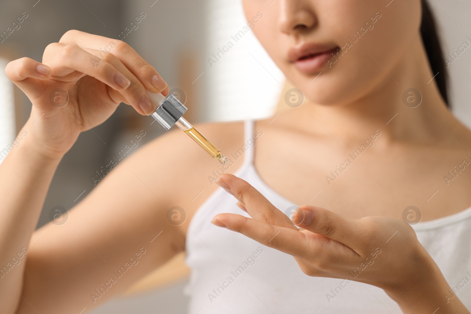 Photo of Beautiful young woman applying cosmetic serum onto her finger in bathroom, closeup