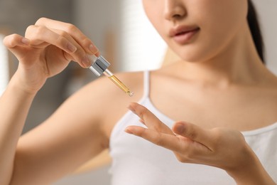 Beautiful young woman applying cosmetic serum onto her finger in bathroom, closeup