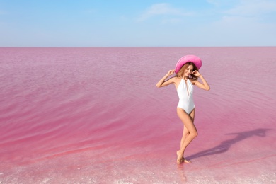 Photo of Beautiful woman in swimsuit posing near pink lake on sunny day