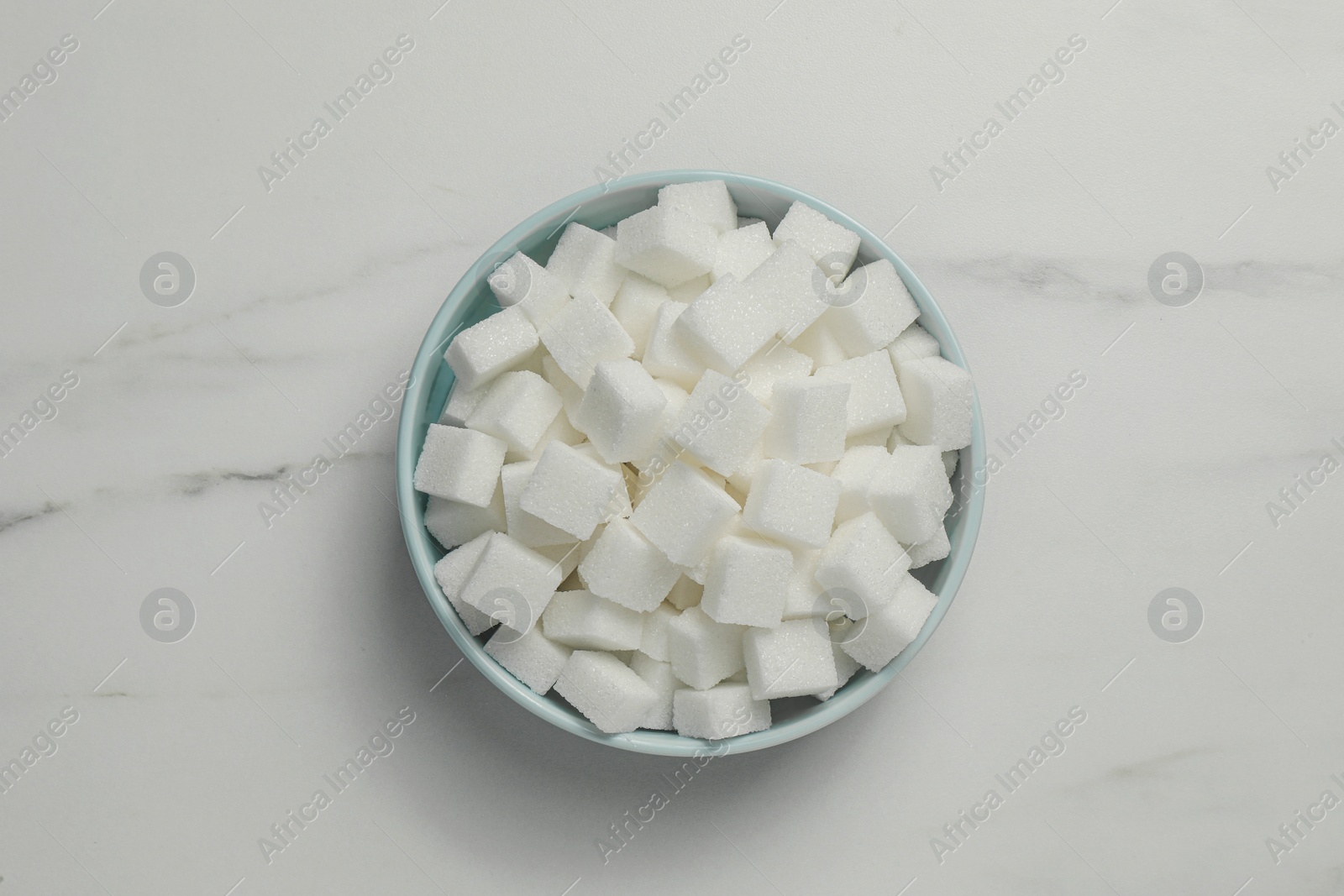 Photo of Bowl of white sugar cubes on marble table, top view