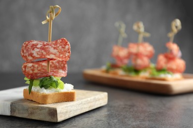 Tasty canapes with salami, greens and cream cheese on grey table, closeup. Space for text