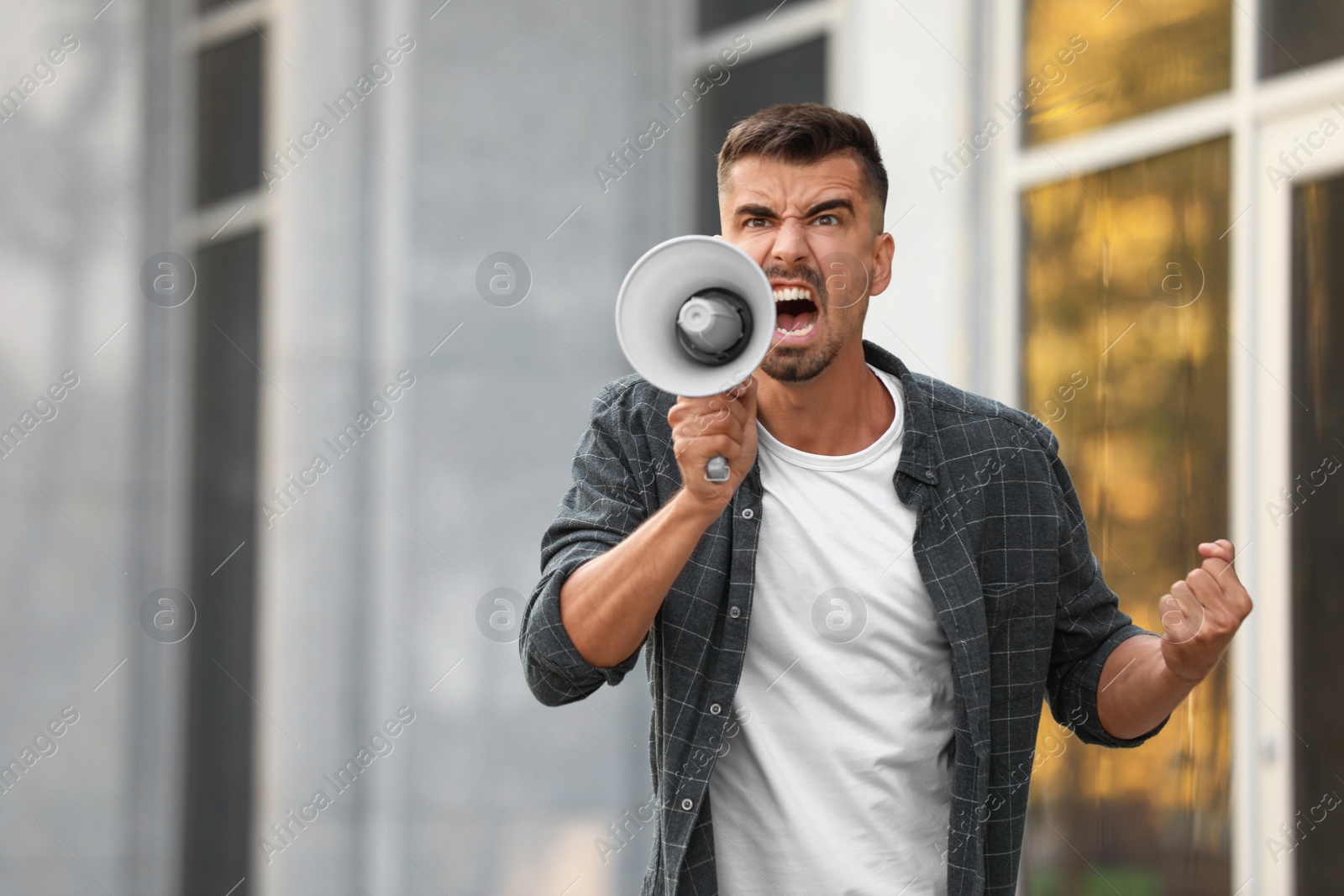 Image of Emotional young man with megaphone outdoors. Protest leader